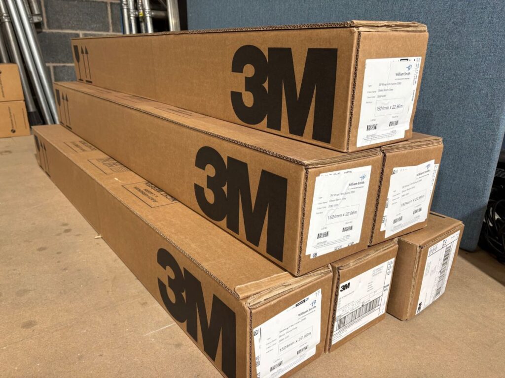 Alt text: Boxes of 3M vinyl wrap rolls stacked in workshop.