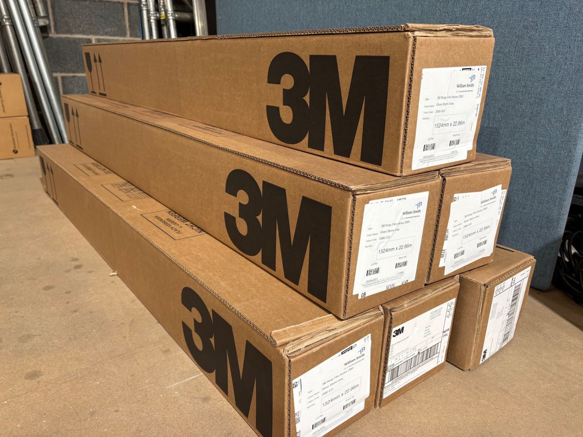 Alt text: Boxes of 3M vinyl wrap rolls stacked in workshop.
