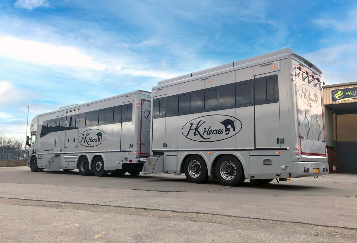The rear view of a silver and white horsebox truck showing double doors, high-visibility LED lighting, and "H-Horse" professional branding.